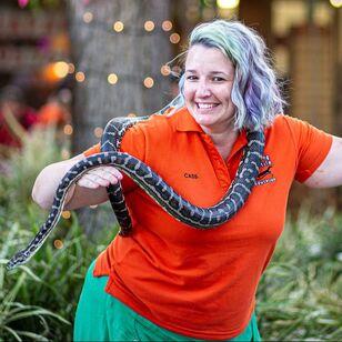 Cass wearing bright colours holding a python and smiling at the camera